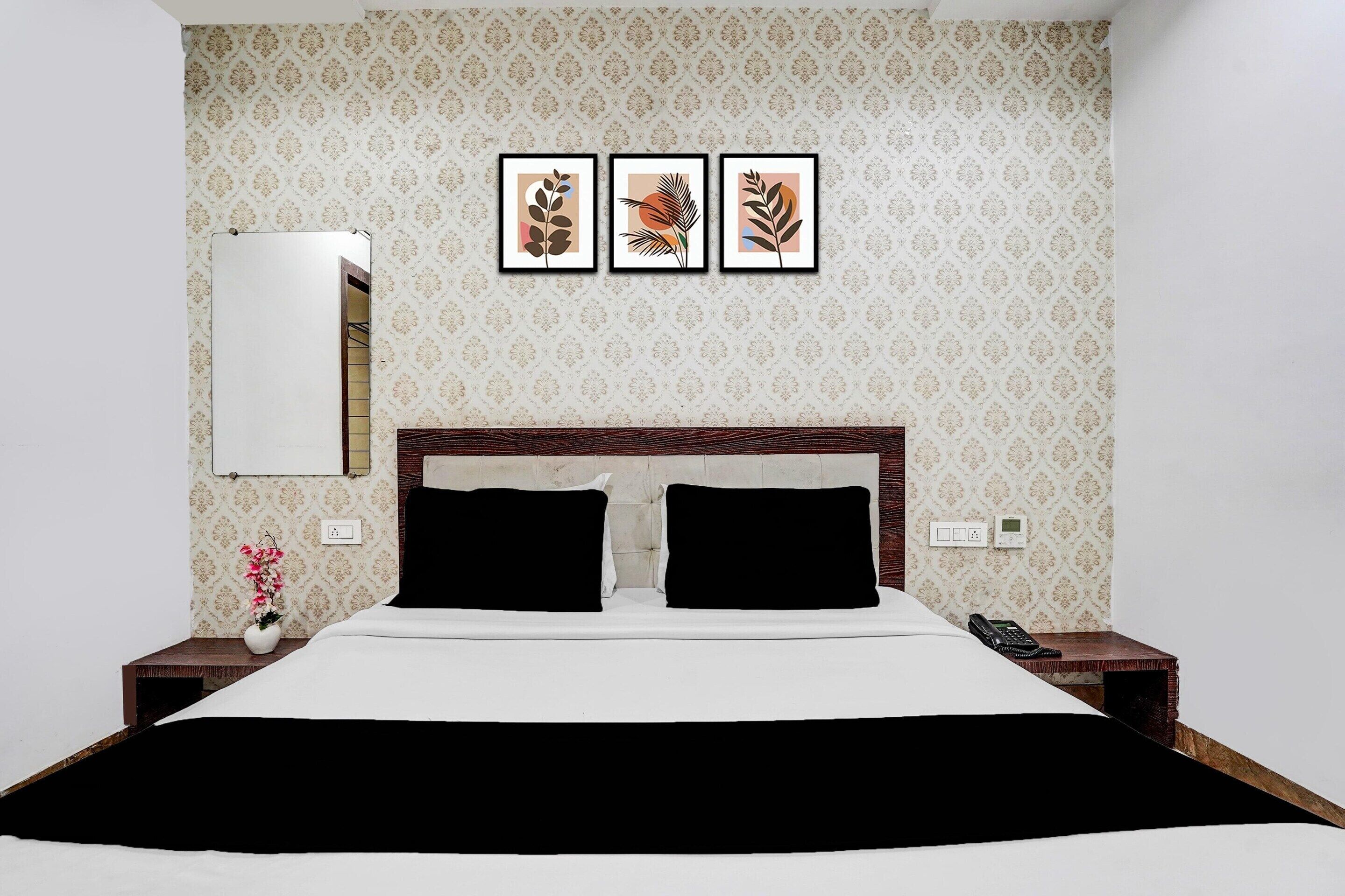 A hotel room with a bed, a nightstand, a phone, a mirror, and three framed pictures on the wall.