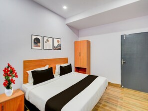 A bedroom with a bed, a nightstand with a vase of flowers, a wardrobe, and three framed pictures on the wall. - Deluxeoyo Nagaram (Hyderabad)
