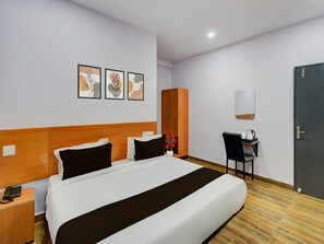 A hotel room with a bed, bedside table, a desk with a chair, a wardrobe, and three framed pictures on the wall. - Deluxeoyo Nagaram (Hyderabad)
