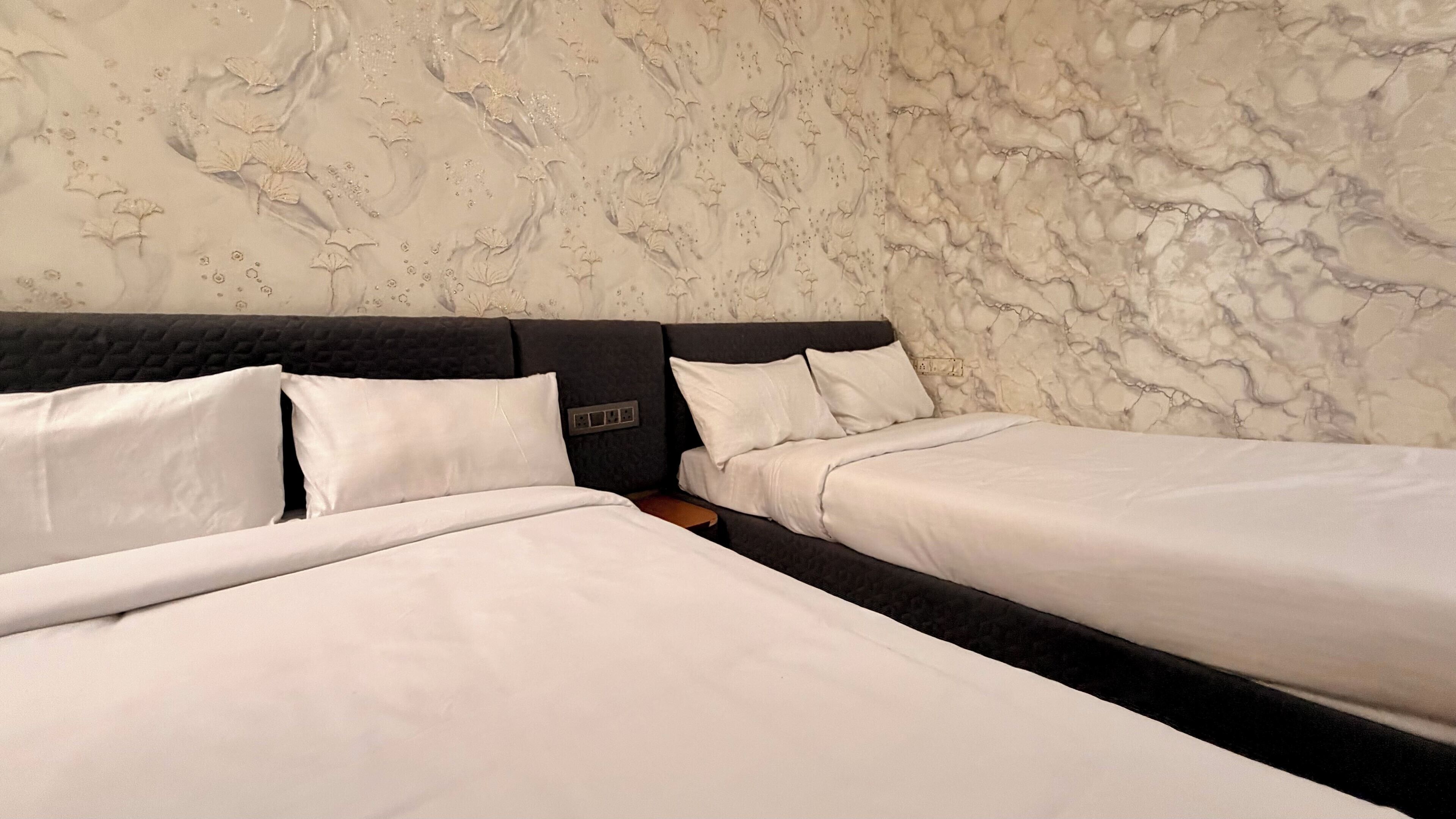 A double bed with a dark headboard, a single bed with a white headboard, and a marble-patterned wall.