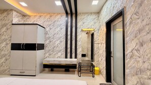A bedroom with a bed, a wardrobe, a vanity with a mirror, and a bathroom with a sink and mirror. - Shubh Kaaraj Resort (Indore)