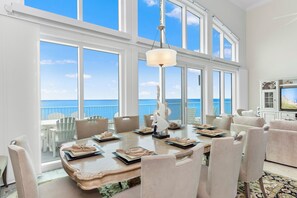 Une salle à manger dotée d’une grande table, de chaises et offrant une vue sur l’océan grâce à de larges fenêtres.