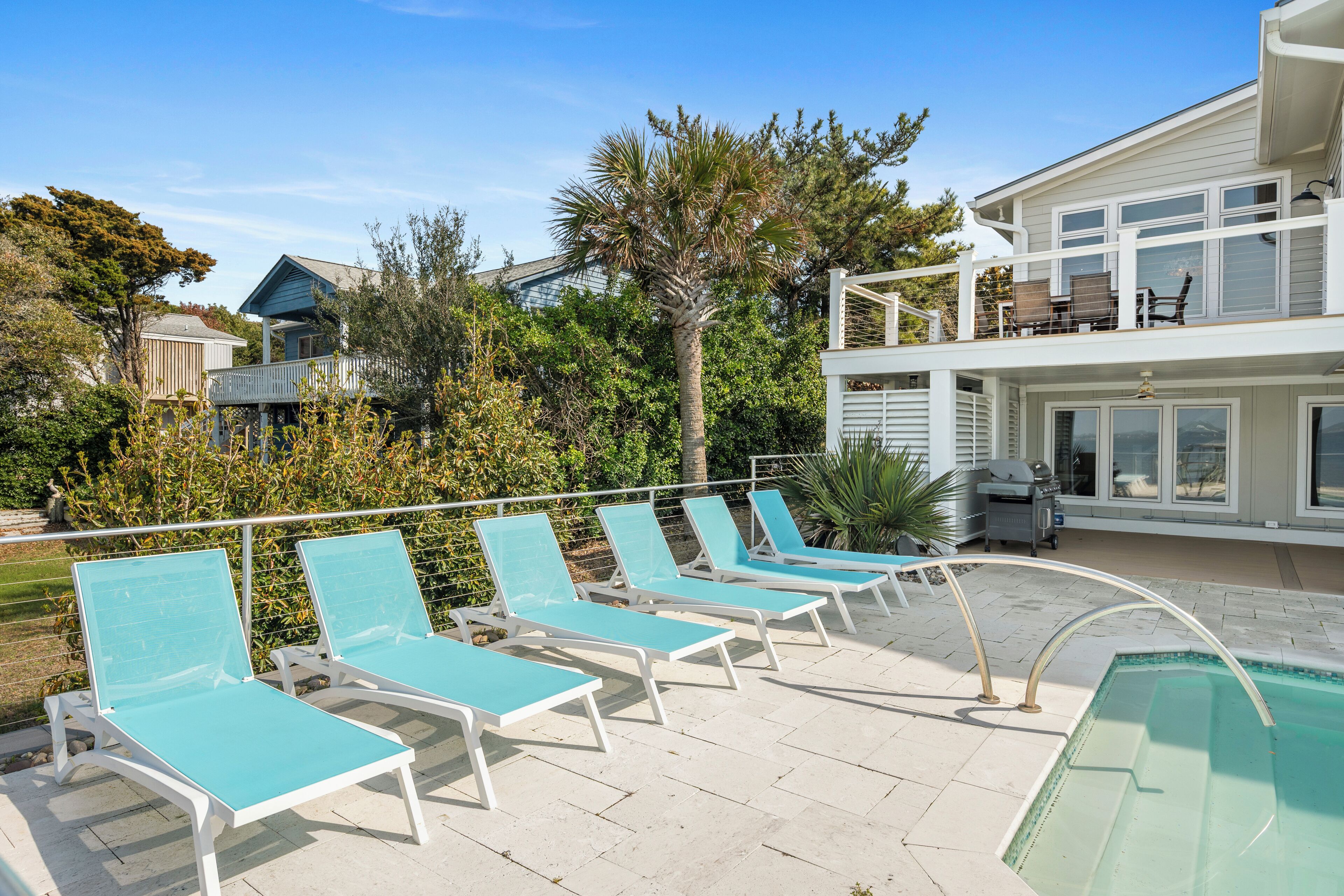 A pool area with lounge chairs, a pool, and a house with a balcony.