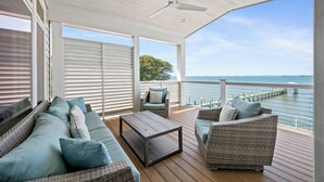 Um terraço coberto ao ar livre com móveis de vime, ventoinha no teto e vista para a água.