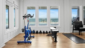 Ginásio em casa com equipamentos de exercício, um banco e vista para o oceano através de grandes janelas.