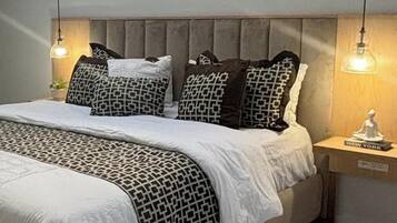 A bedroom with a skylight, a bed with patterned bedding, a headboard, bedside lamps, and a nightstand with a book.