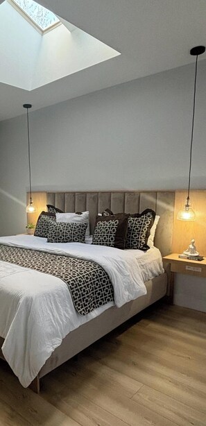 A bedroom with a skylight, a bed with patterned bedding, a headboard, bedside lamps, and a nightstand with a book.