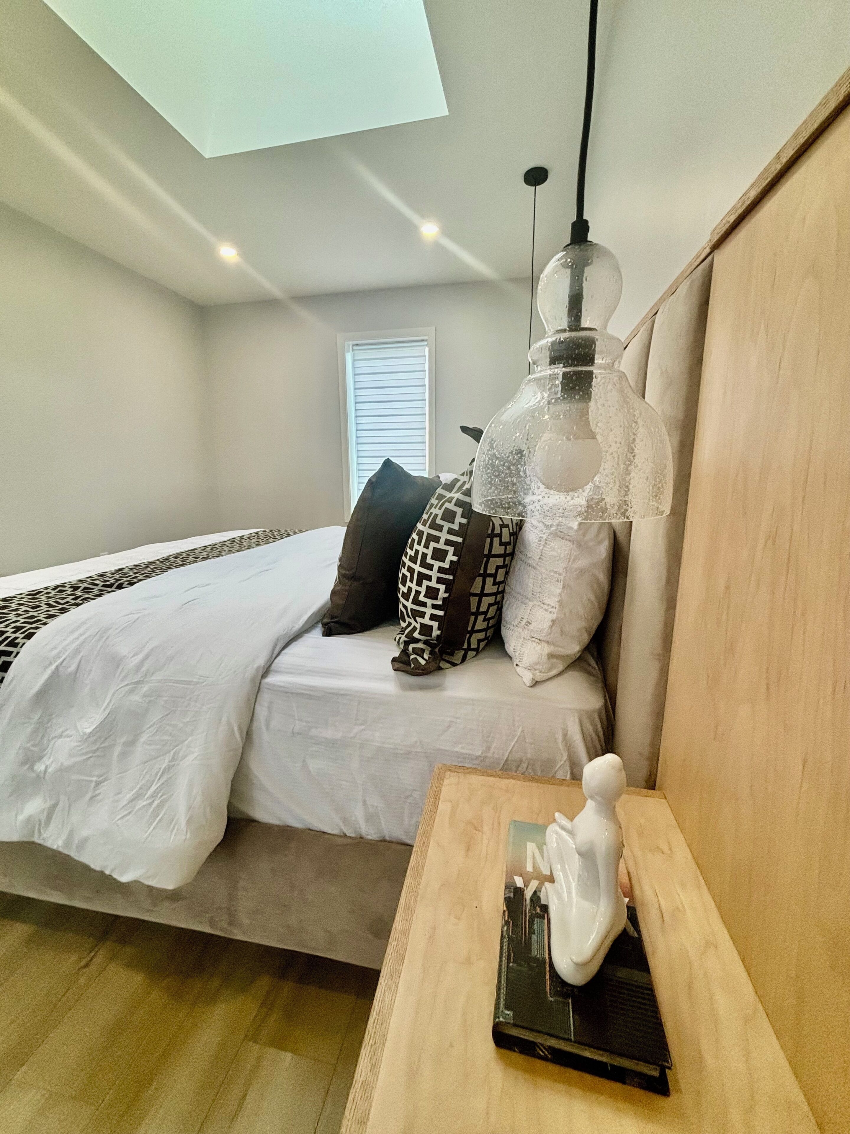 A bedroom with a bed, pillows, a nightstand, a lamp, and a skylight.