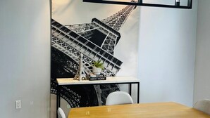 Un'area pranzo con un tavolo in legno, quattro sedie, una lampada a sospensione con cornice nera e un grande poster in bianco e nero della Torre Eiffel appeso al muro.