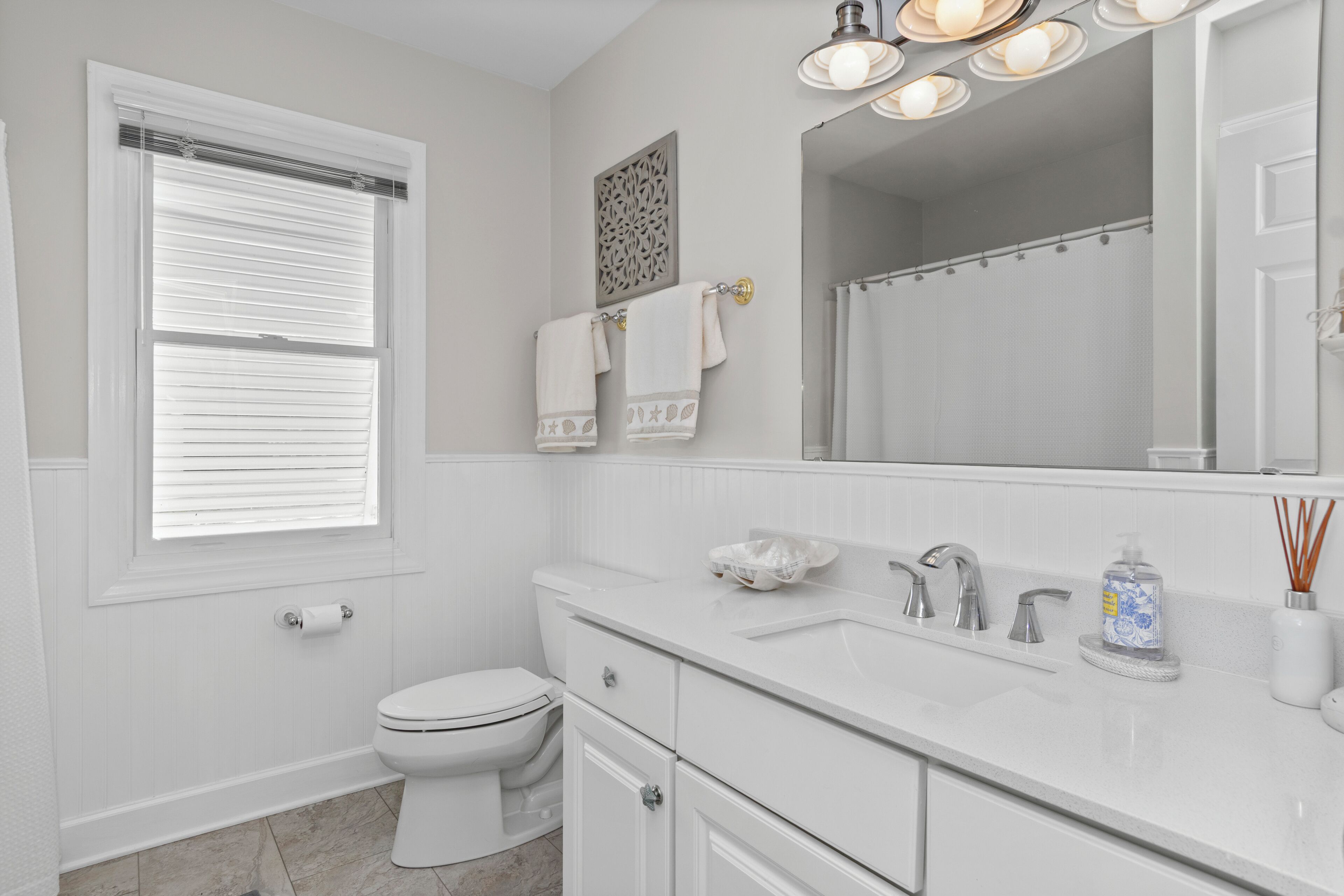 A bathroom with a toilet, sink, mirror, and window with blinds.