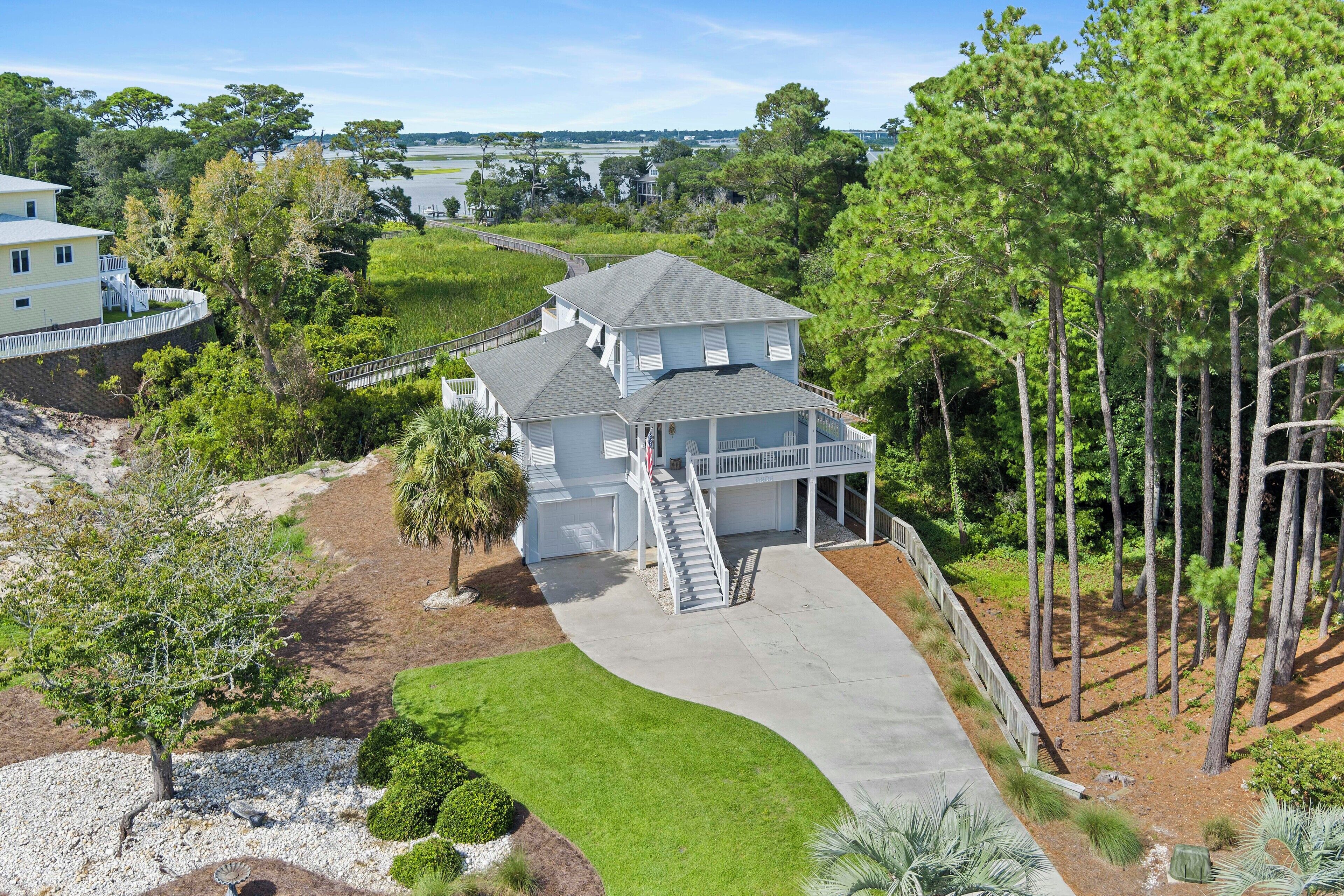 A two-story house with a covered porch, a driveway, and a surrounding landscape with trees and a body of water.