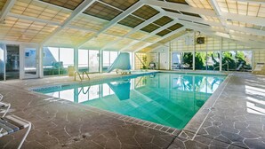 Una piscina interior con suelo de baldosas, techo de cristal transparente y vistas al exterior.