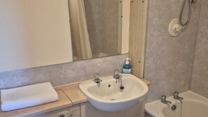 Ein Badezimmer mit Waschbecken, Spiegel, Dusche, Toilette und Mülleimer.