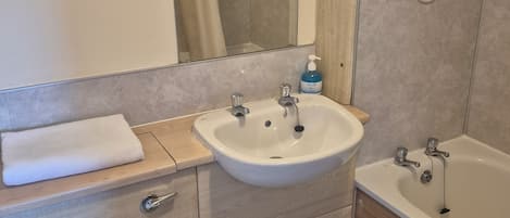 Ein Badezimmer mit Waschbecken, Spiegel, Dusche, Toilette und Mülleimer.