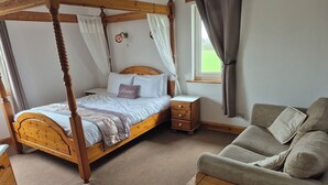 Ein Himmelbett mit Baldachin, ein Nachttisch, ein Sessel und ein kleiner Tisch.