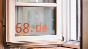 Ein Fenster, durch dessen Glas der Text '68.de' zu sehen ist.