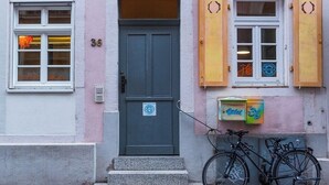 Ein Gebäude mit einer grauen Tür, einem Fenster mit orangefarbenen Verzierungen und einem Fahrrad davor.