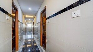 A hallway with a reflective floor, doors, and a light switch on the wall. - Deluxehotel Lanco Hills (Hyderabad)