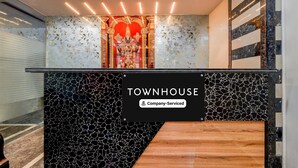 A reception area with a mosaic wall, a sign reading 'TOWNHOUSE Company-Serviced,' and a staircase leading to the upper floor. - Deluxehotel Lanco Hills (Hyderabad)