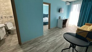 Una habitación con cama, escritorio, silla, una mesita y baño con inodoro y lavamanos.