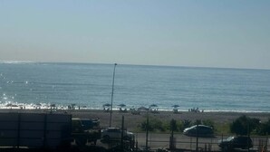 Vista de playa con sombrillas, una calle y cielo despejado.