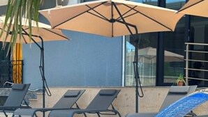 Una piscina con fuente, sillas de descanso y sombrillas.