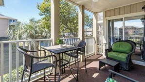A covered outdoor area with a table and chairs, a green cushioned chair, and a view of the surrounding landscape. - Tilghman Shores H1- 2 Bedroom- Short Walk To Beach (North Myrtle Beach)