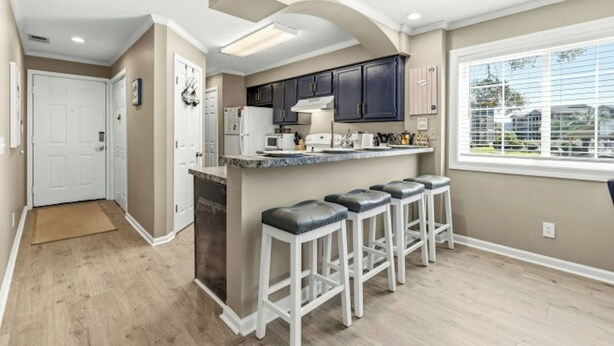 A kitchen with dark cabinets, a white refrigerator, and a window with blinds. - Tilghman Shores H1- 2 Bedroom- Short Walk To Beach (North Myrtle Beach)