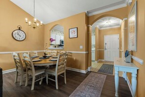 Un comedor con una mesa y sillas de madera, un reloj en la pared y un pasillo que conduce a una puerta.