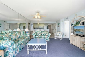 A living room with floral-patterned sofas, a small table, and a ceiling fan. - Emerald Cove II 7B- Oceanfront 3BR-Outdoor Pool (North Myrtle Beach)