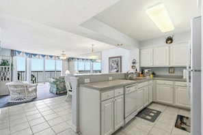 A kitchen with white cabinets, a large island, and a view to the outside. - Emerald Cove II 7B- Oceanfront 3BR-Outdoor Pool (North Myrtle Beach)