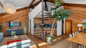A spacious loft with a wooden interior, a spiral staircase, a dining area, and a kitchen. - Oceanfront Treehouse Retreat | Private Beach Walkw (Pine Knoll Shores)