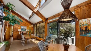 A spacious dining area with wooden tables and chairs, large windows, and a ceiling with exposed beams. - Oceanfront Treehouse Retreat | Private Beach Walkw (Pine Knoll Shores)