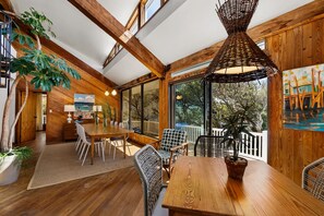 A spacious dining area with wooden tables and chairs, large windows, and a ceiling with exposed beams.