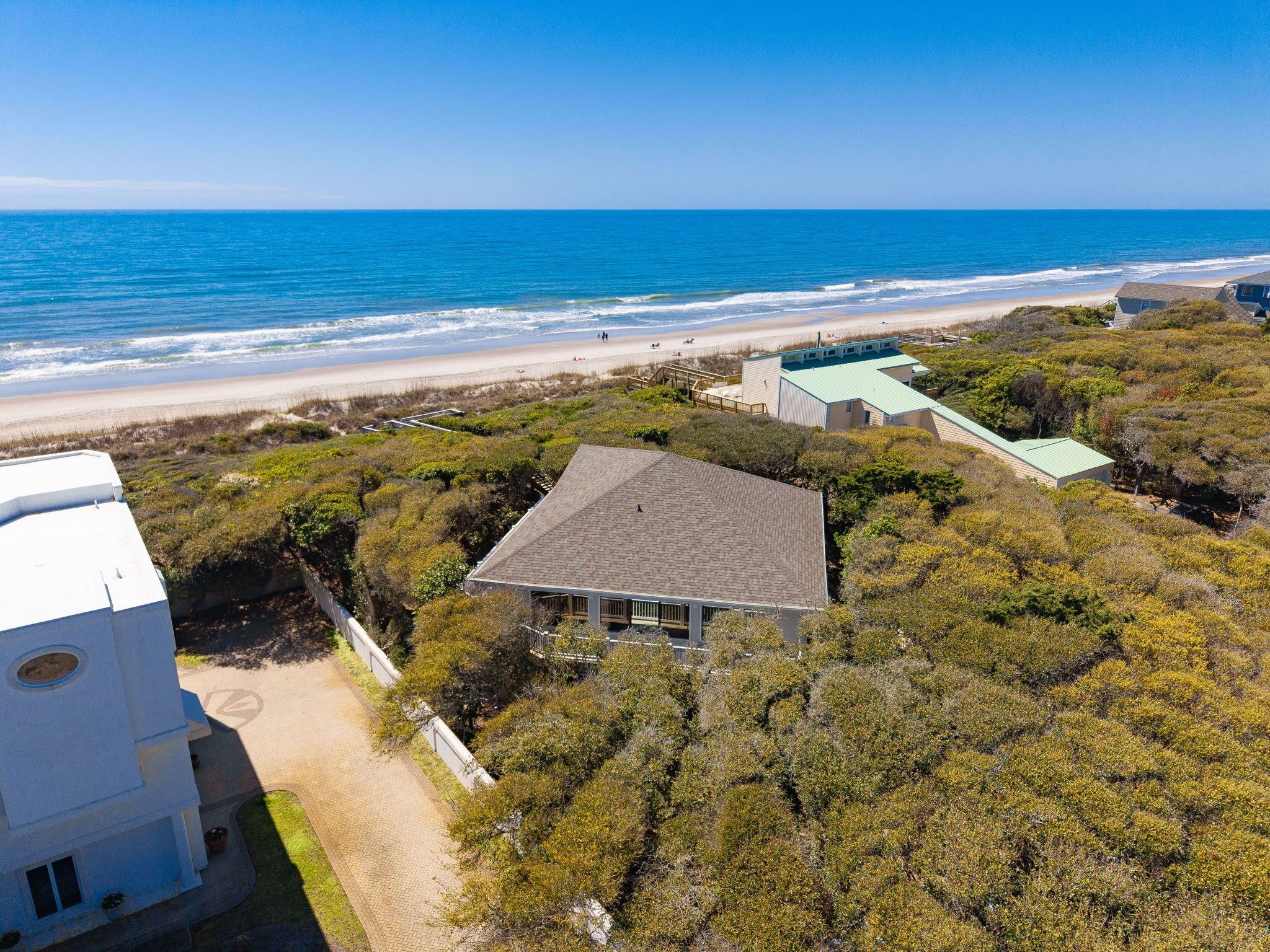 An aerial view of a coastal property with a beach, a small building with a tiled roof, and a white building with a circular window.