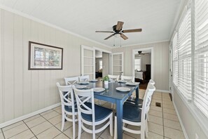 A dining area with a blue table, white chairs, a ceiling fan, and a framed picture on the wall. - 1 Sandy Shore- Oceanfront 6BR House- Cherry Grove (North Myrtle Beach)