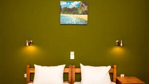 Un dormitorio con una cama, dos lámparas de pared, una mesita de noche y un cuadro de una playa.