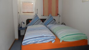 Un letto singolo con lenzuola a righe, un comodino con una lampada e una finestra con tenda.