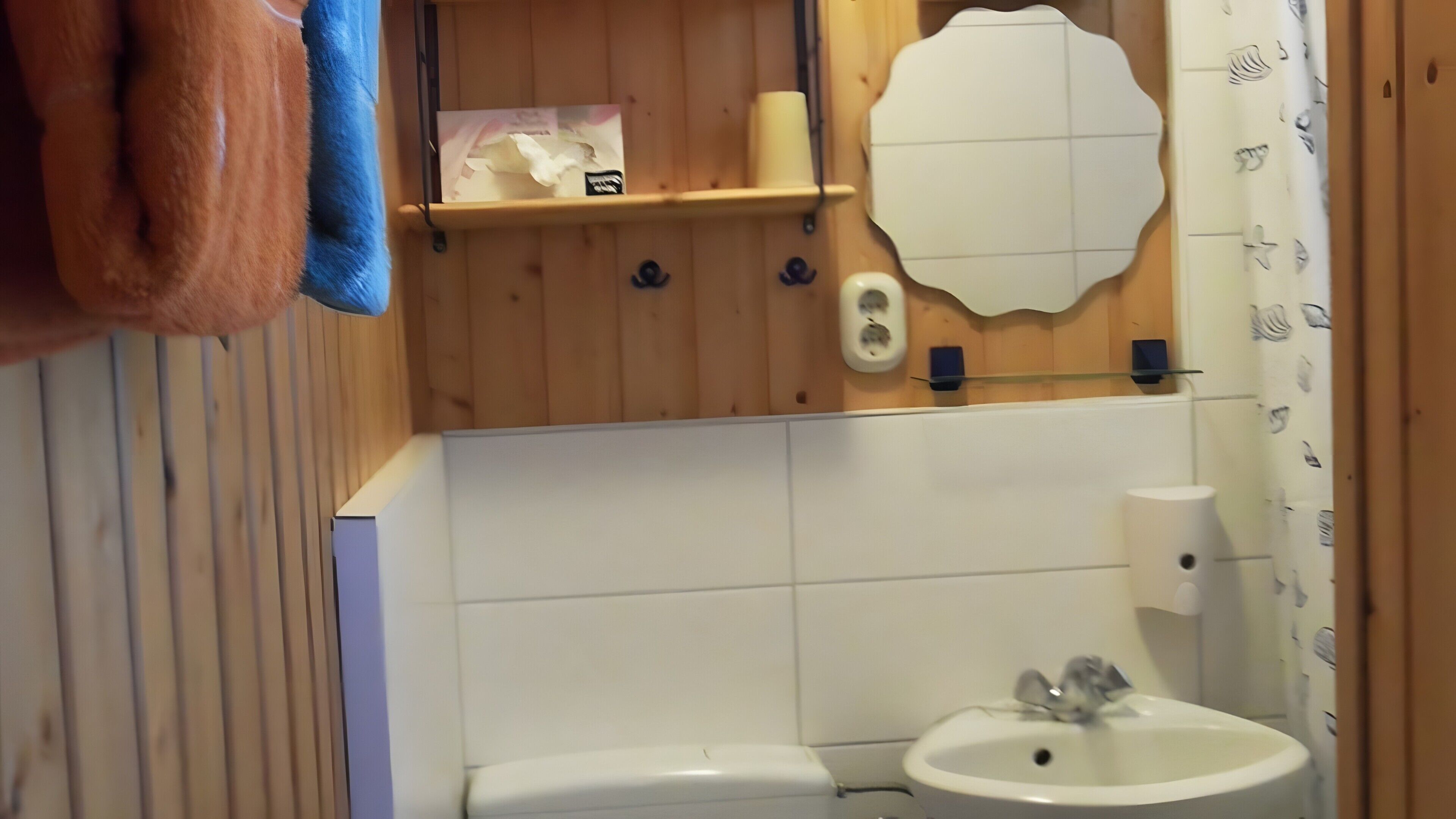 Une salle de bain équipée de toilettes, d’un lavabo, d’un miroir, d’un porte-serviettes et d’une étagère contenant des articles de toilette.
