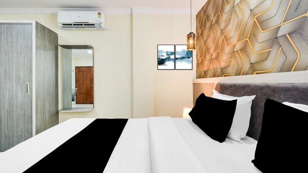 A modern hotel room with a bed, a wardrobe, a mirror, and a wall-mounted air conditioner. - Deluxe Hotel Blue Petals (Hyderabad)