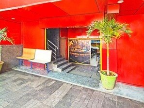 A red building entrance with a bench, stairs, and a potted plant. - Deluxemedipally (Hyderabad)