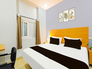 Ein Hotelzimmer mit Bett, Schreibtisch, Stuhl, einem Fenster mit Vorhängen und Wandbildern.