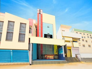 A multi-story building with a prominent vertical red and blue stripe, a storefront with a sign, and a staircase leading to an upper level. - Deluxemedipally (Hyderabad)