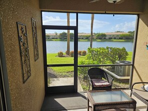 A room with a large sliding glass door leading to a view of a lake, a wicker chair, and a small table. - 3-bedrooms townhouse in lovely Verandah Fort Myers Florida (Fort Myers)