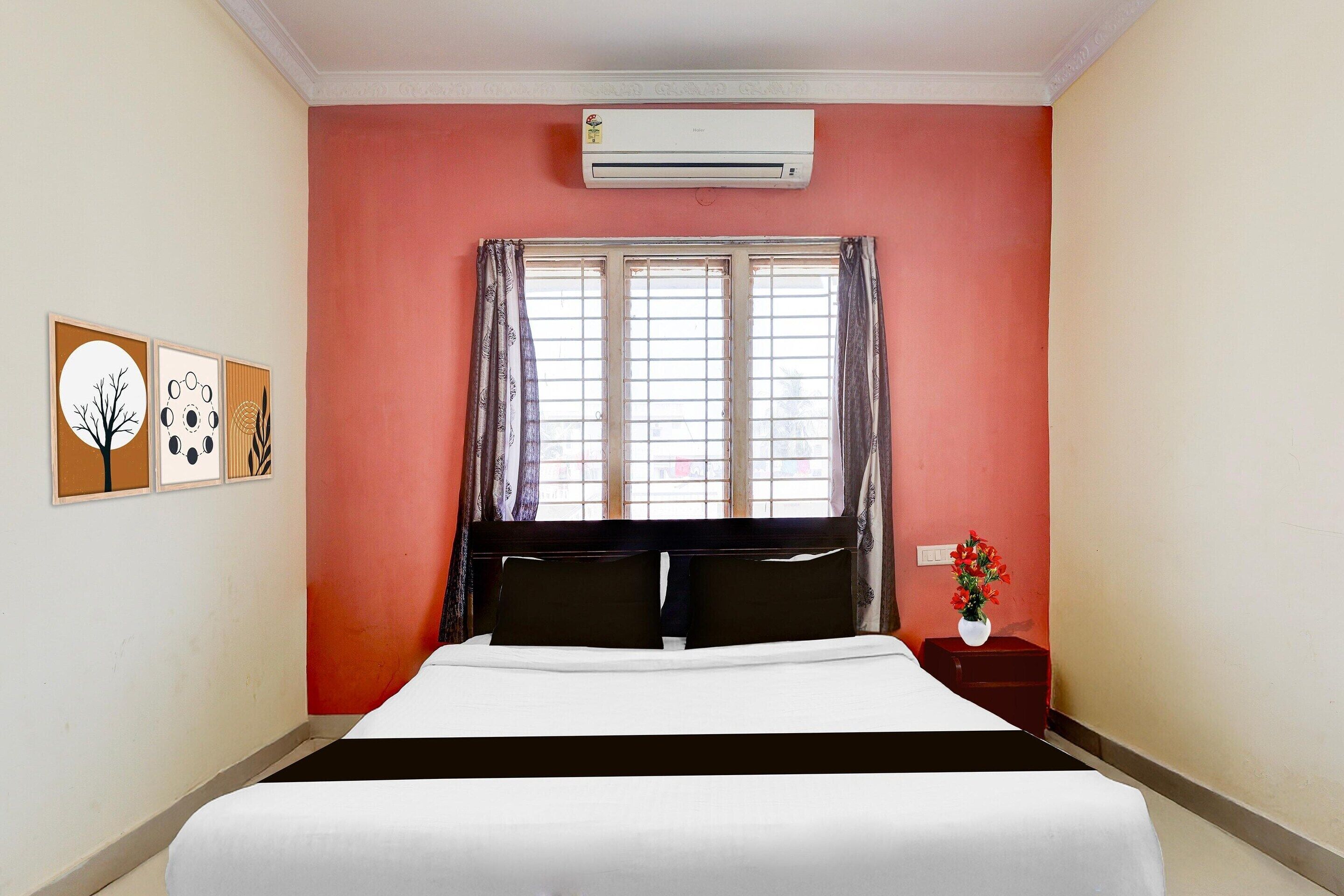 Una habitación de hotel con cama, aire acondicionado, ventana con cortinas y decoración en la pared.