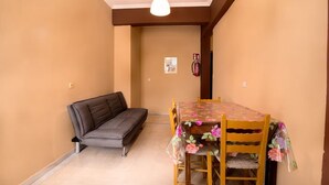 A room with a sofa, a dining table with chairs, a hanging light fixture, and a fire extinguisher on the wall. - Southgate 3 by MPS (Agios Georgios)