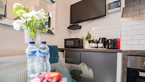 A modern kitchen with a glass table, two water bottles, a vase with white flowers, and a coffee maker. - Bright Studio | Walk to City | Washer & Dryer (Dublin)