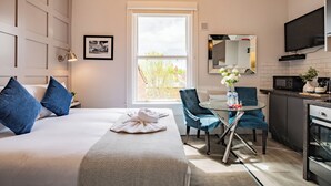 A hotel room with a bed, a dining table with chairs, a kitchen area, and a large window. - Bright Studio | Walk to City | Washer & Dryer (Dublin)