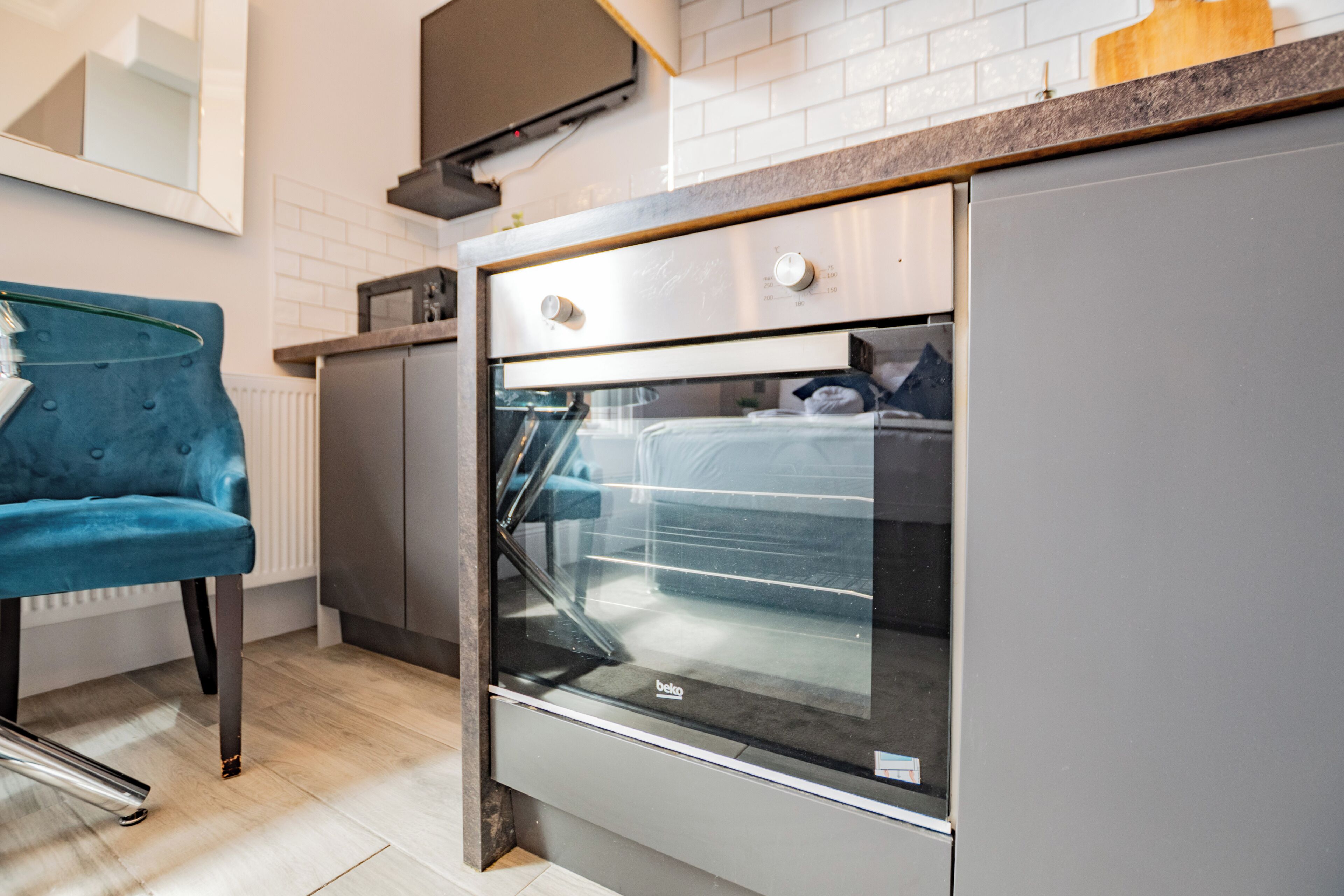 Een moderne keuken met een ingebouwde oven, een blauwe stoel en een houten aanrecht.