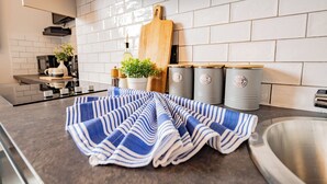 A kitchen with white tiles, a striped towel, a wooden cutting board, and stainless steel appliances. - Bright Studio | Walk to City | Washer & Dryer (Dublin)